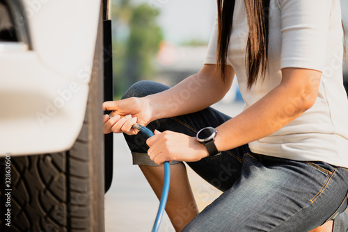 Woman driver checking air pressure and filling air in the tires close up.