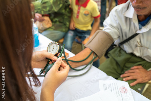 Volunteer nurse measuring blood pressure of poor Asian people outdoors closeup