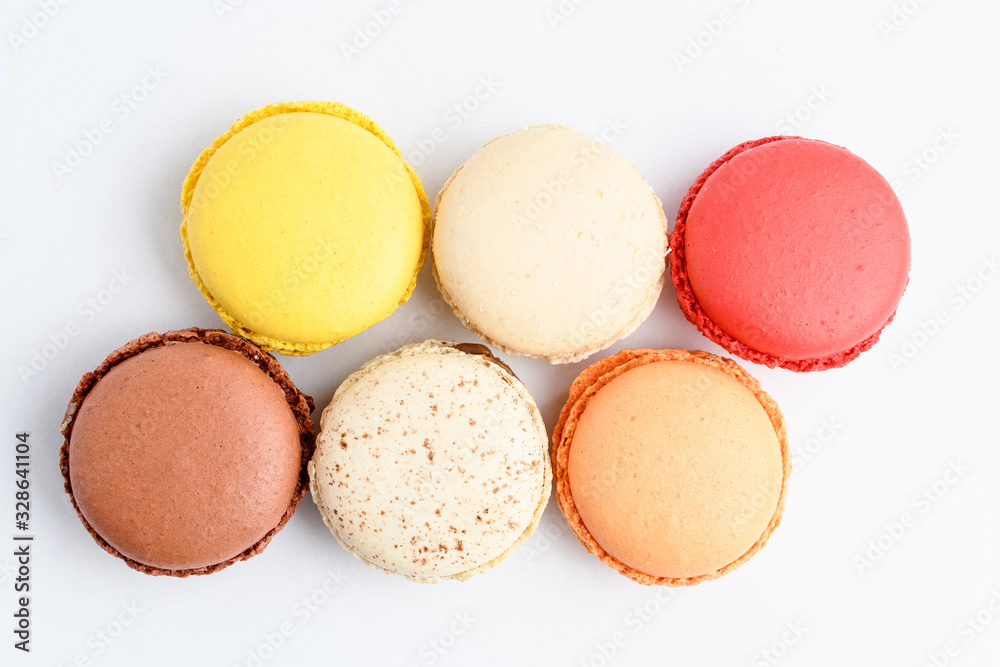 Top view of six sweet French macarons with different aromas, isolated on white, flavours of lemon, caramel, vanilla, orange and chocolate, tasty dessert in pastel colors on a table Top view of six sweet French macarons with different aromas, isolated on white, flavours of lemon, caramel, vanilla, orange and chocolate, tasty dessert in pastel colors on a table