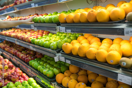 Fresh healthy fruits on shelves in supermarket. With a woman hand choosing best fruits