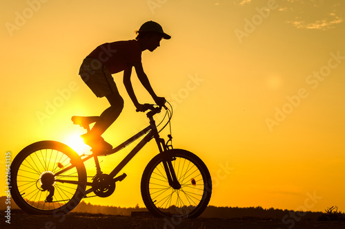 Boy   kid 10 years old riding bike in countryside  teenager making trick on bycicle  silhouette of riding person at sunset in nature
