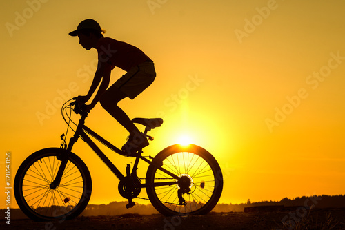 Fototapeta Naklejka Na Ścianę i Meble -  Boy , kid 10 years old riding bike in countryside, teenager making trick on bycicle, silhouette of riding person at sunset in nature