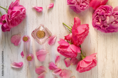 Rose water and oil in glass bottle and fresh flowers on branch on wooden background, SPA and aromatherapy concept