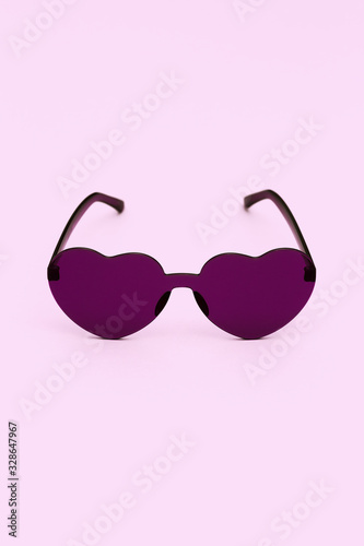 Minimal style fashion photography with heart shaped glasses on pink background. Violet modern sunglasses. Trendly summer concept. Copy space.
