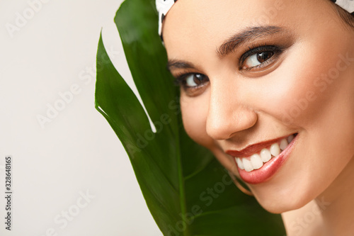 Beautiful African-American woman with tropical leaf on light background