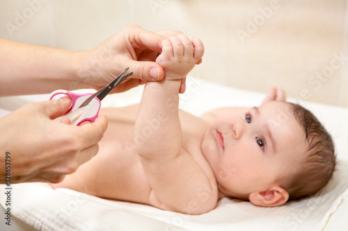 Baby getting fingernails cut by his mother with scissors while lying on his back. Nursing a child © Kekyalyaynen