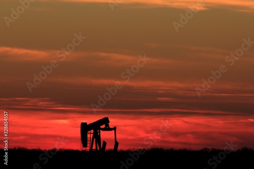 Kansas colorful Sunset clouds and an Oilwell Pump with tree's out in the country.