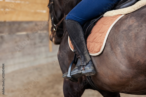 Closeup of a woman in riding gear sitting in a saddle on a brown horse on the training ground