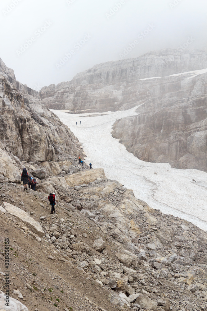 People hiking towards col Bocca del Tuckett on snow field in Brenta Dolomites mountains, Italy