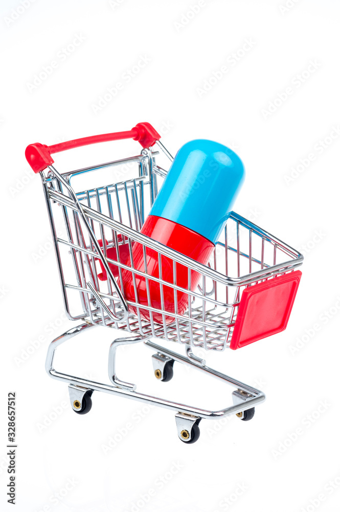 Miniature shopping cart carrying large pill capsule on white background
