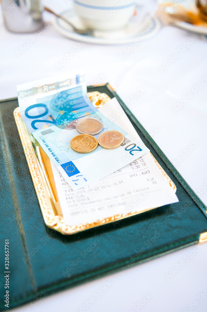 Obraz premium Tray of euro notes and coins sitting in a tray on an outdoor table with a nondescript restaurant receipt in Portuguese