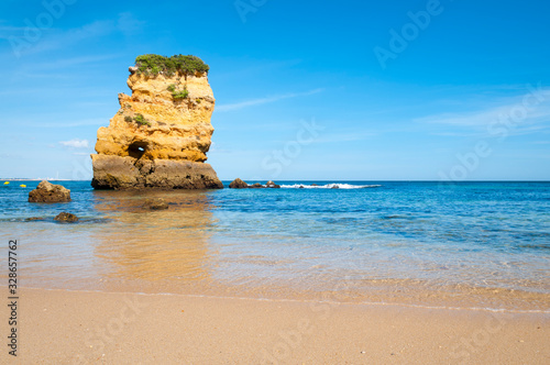 Bright sunny view of dramatic sea stack rock at Dona Ana beach near Lagos, in the Algarve section of southern Portugal