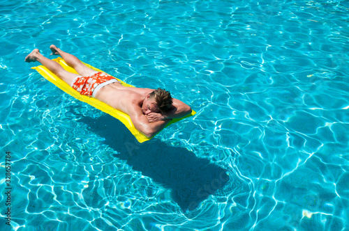 Unrecognizable man in colorful swim shorts floating on an inflatable lilo on a bright blue swimming pool
