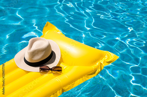 Sun hat and sunglasses resting on bright yellow inflatable raft floating in blue swimming pool photo