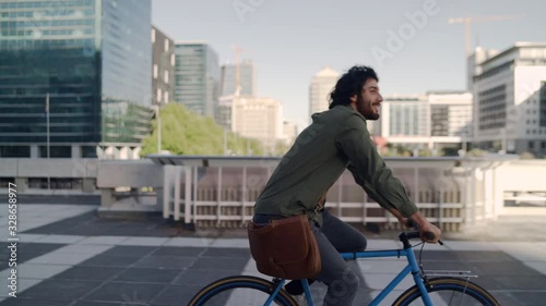 Successful smiling professional young man riding bicycle in front of modern buildings at background