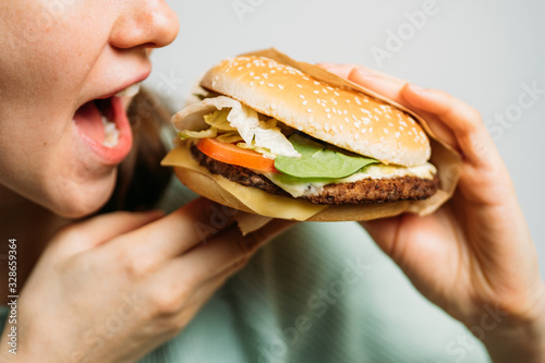 The girl holds a hamburger with her hands and eats it with appetite.