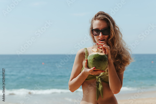 The girl with the coconut on the beach. Girl drinks coconut milk on the beach. High quality photo