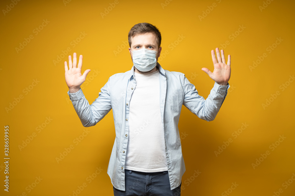 Calm man in a medical mask on face, wants to avoid the spread of the virus through touch, he raised hands and looks in the camera. Calm man in a medical mask on face, wants to avoid the spread of the virus through touch, he raised hands and looks in the camera.