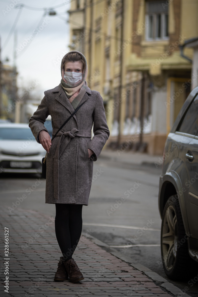 Young attractive woman in protective medical mask stands near a car. Protection against viruses - influenza, coronavirus  and smog