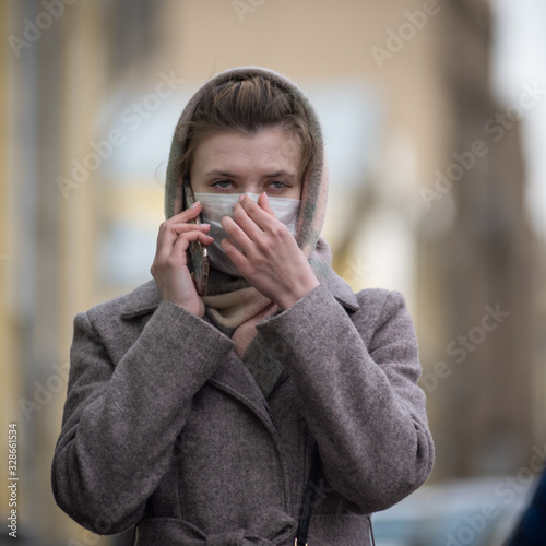 Young attractive woman in a medical protective mask is talking on the phone in the street. Protection against viruses - influenza, coronavirus and smog