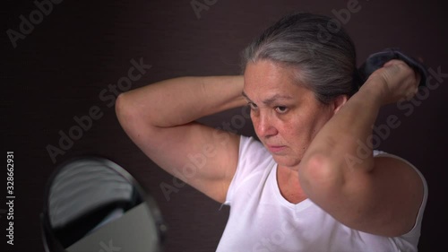 Woman tying her long gray hair in ponytail, making hairdo at home