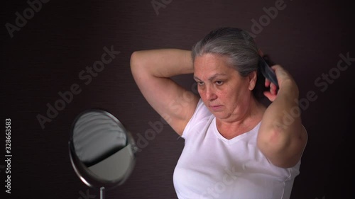 Older woman doing long hair style looking in mirror, ponytail hairstyle at home