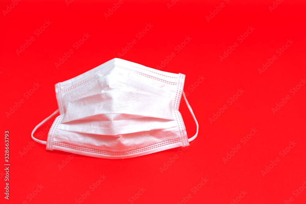 White surgical mask to help protect against the corona virus and other contagious diseases. Copy space. Horizontal shot. Isolated on red background. White surgical mask to help protect against the corona virus and other contagious diseases. Copy space. Horizontal shot. Isolated on red background.