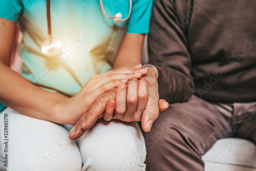 Female carer consoling a senior patient at the nursing home. Closeup shot of a young woman holding a senior man's hands in comfort. Female healthcare worker holding hands of senior man at care home photo