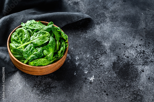 Fresh spinach leaves in a wooden bowl. Black background. Top view. Copy space