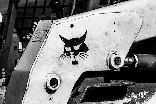 lose-up of a small earth-moving machine known as a Bobcat. The image is in b&w, is gritty from the dirt, and shows a stylized bobcat head.