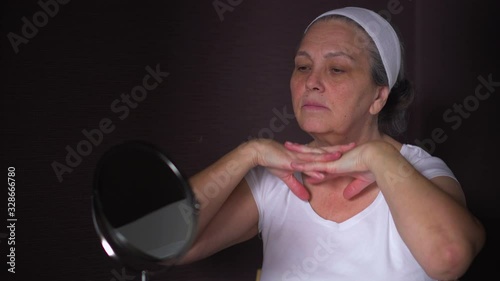 Senior woman looking at reflection in mirror do face lift massage