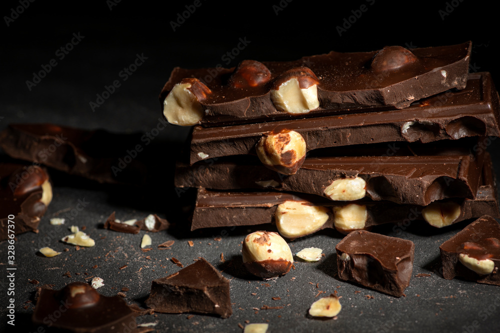 Pieces of chocolate with a nuts tied with a white and red   lying on a dark texture table.