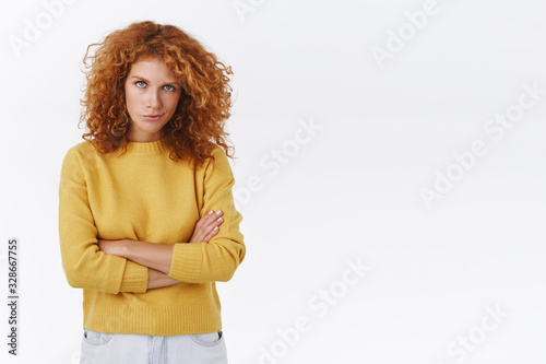 Hideous curly redhead woman have evil sly plan, smirk and look from under forehead, frowning, cross arms over chest, staring assertive and devious, make cunning smile, white background photo