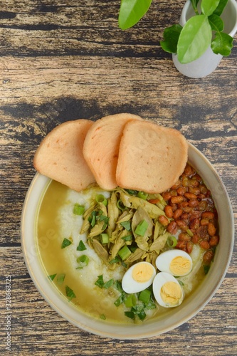 Bubur Ayam, Indonesian rice congee with shredded chicken, scallion, celery, fried soybean, boiled quail egg, yellow chicken broth and kerupuk photo