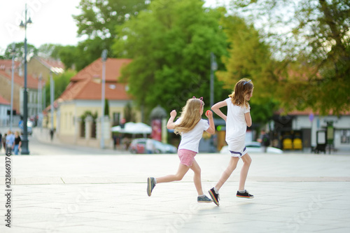 Two cute young sisters having fun together on beautiful summer day in a city. Active family leisure with kids.
