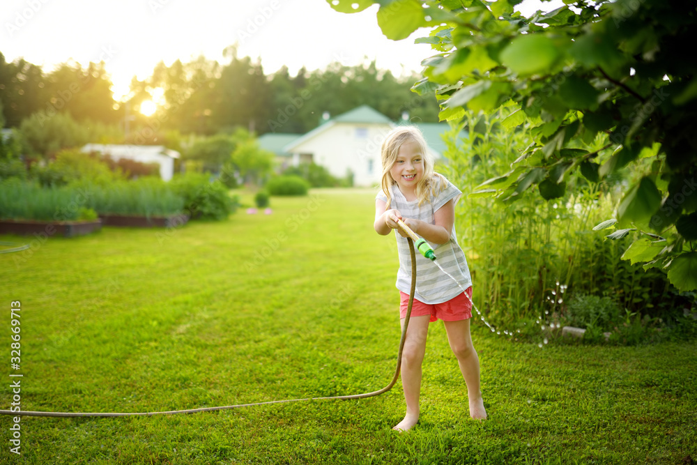 Adorable little girl playing with a garden hose on warm summer day. Outdoor activities for kids. Adorable little girl playing with a garden hose on warm summer day. Outdoor activities for kids.