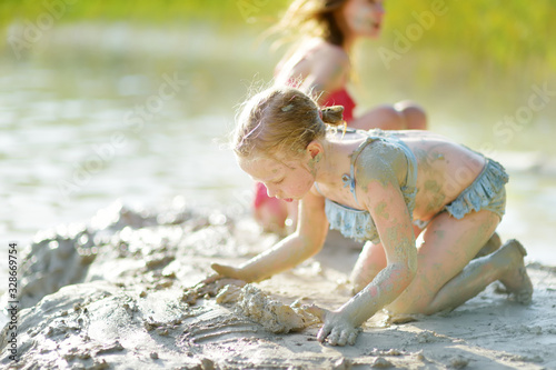 Two young sisters taking healing mud baths on lake Gela near Vilnius  Lithuania. Children having fun with mud. Kids playing with clay.