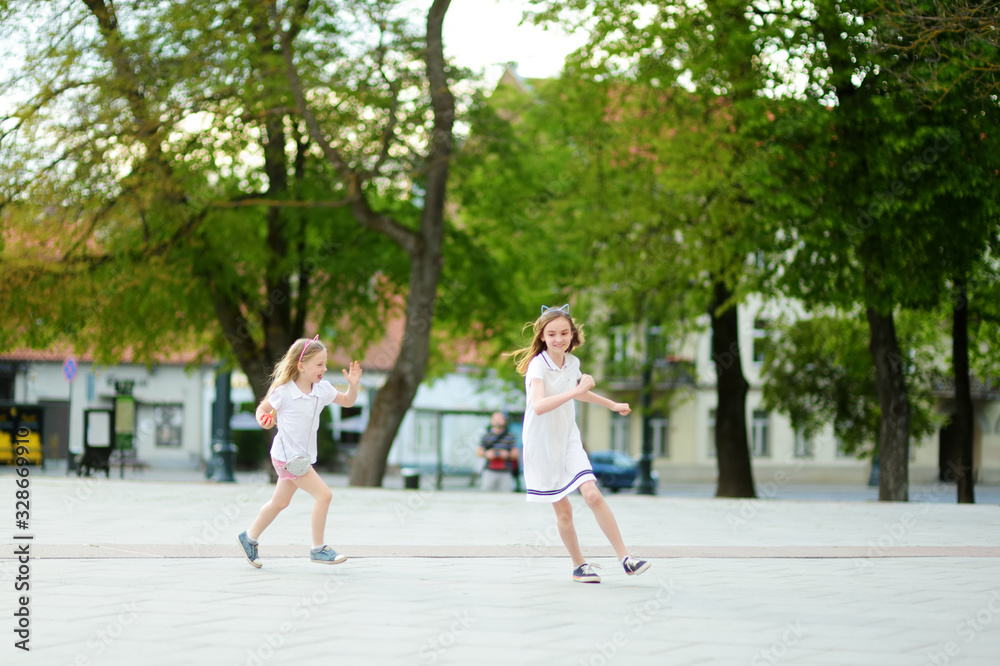 Two cute young sisters having fun together on beautiful summer day in a city. Active family leisure with kids. Two cute young sisters having fun together on beautiful summer day in a city. Active family leisure with kids.