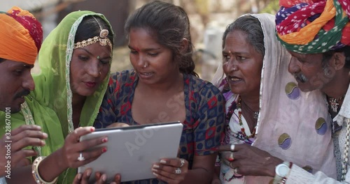 Family in rural setting holding a touch screen tablet as they have an animated discussion and enjoying the capabilities and reach of the wireless wifi network sitting in their village, back of beyond  photo