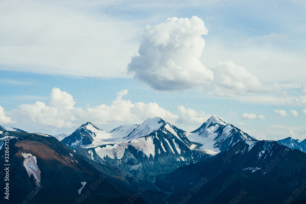 Atmospheric alpine landscape with huge cloud above giant mountains with glaciers. Meltwater streams flow from snowy rocks. Glacial creek on highland valley. Wonderful aerial scenery on high altitude.