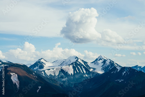 Atmospheric alpine landscape with huge cloud above giant mountains with glaciers. Meltwater streams flow from snowy rocks. Glacial creek on highland valley. Wonderful aerial scenery on high altitude.