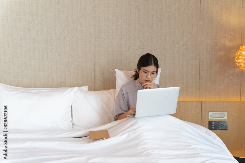Young asian woman relaxing in the hotel and working with laptop on a bed, Business trip, Working travel concept Young asian woman relaxing in the hotel and working with laptop on a bed, Business trip, Working travel concept