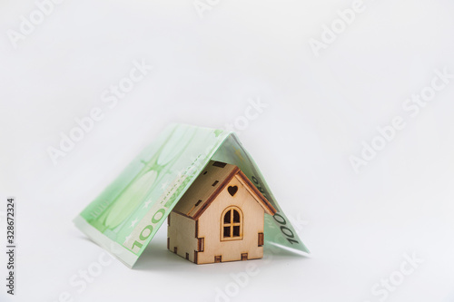 Financial growth concept, real estate tax, buying and selling houses, insurance. A miniature house and a banknote like a roof. Protect your house concept. Small toy house covered by dollars and euros