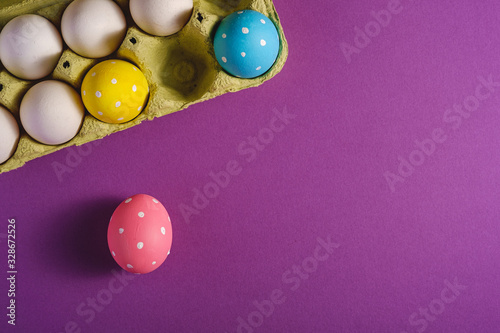 Colorful polka dot Easter eggs in egg tray on purple violet plain background, greeting card, copy space, top view