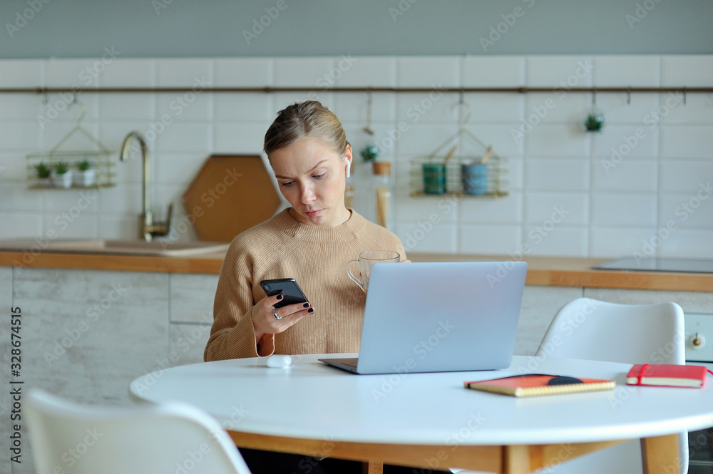 Lovely blonde woman working with her laptop while sitting in the kitchen in her apartment Lovely blonde woman working with her laptop while sitting in the kitchen in her apartment
