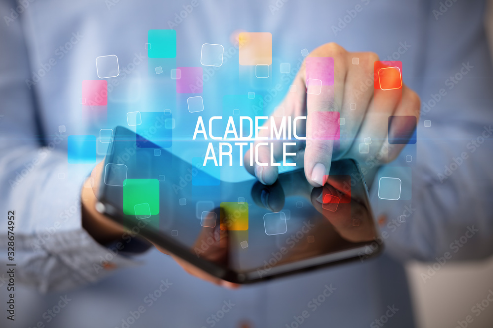 Young man holding a foldable smartphone with ACADEMIC ARTICLE inscription, educational concept Young man holding a foldable smartphone with ACADEMIC ARTICLE inscription, educational concept