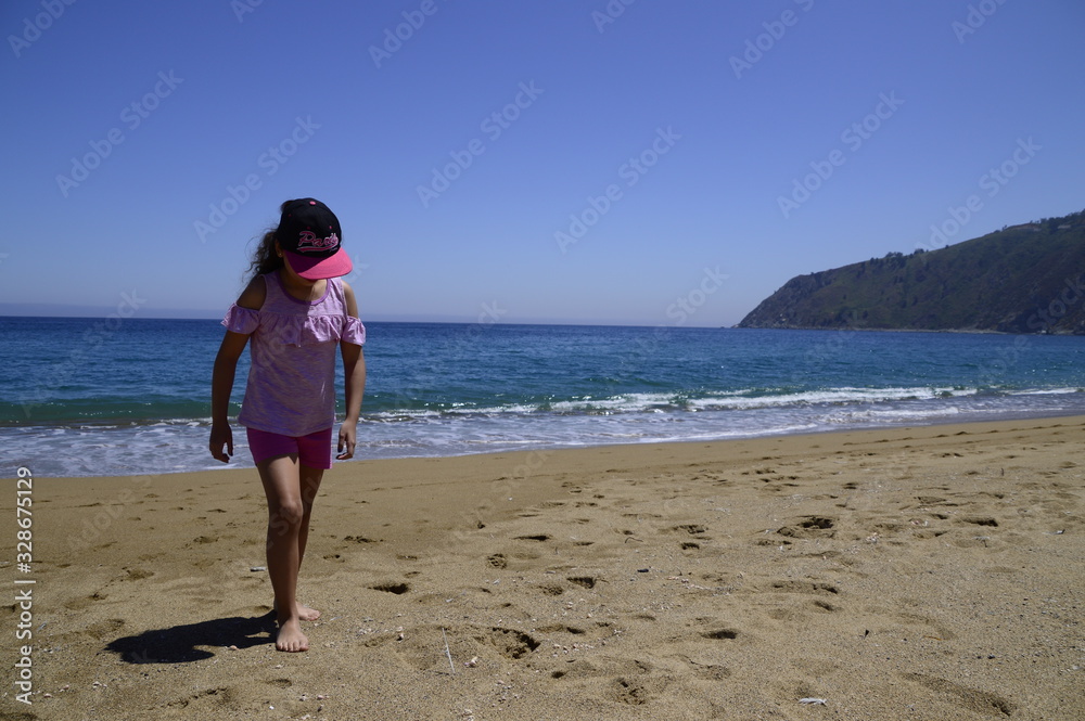 niña sola caminando a orillas del mar