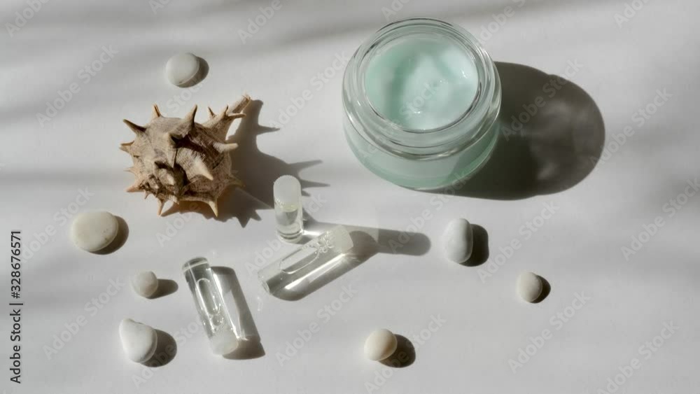 Natural self-care cosmetic set. Glass jar with natural moisturizing cream, bottles of hyaluronic acid, cosmetic serum, seashell and white sea stones in morning sun rays. Facial skincare SPA concept. Natural self-care cosmetic set. Glass jar with natural moisturizing cream, bottles of hyaluronic acid, cosmetic serum, seashell and white sea stones in morning sun rays. Facial skincare SPA concept.