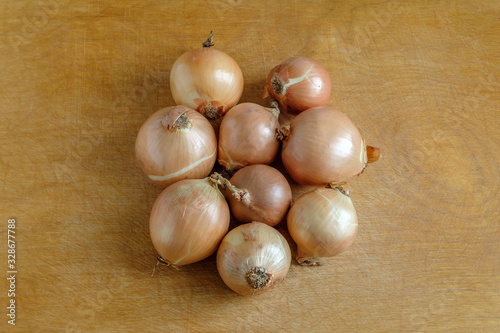 Yellow onions of different sizes and shapes lie in the center on a wooden table.