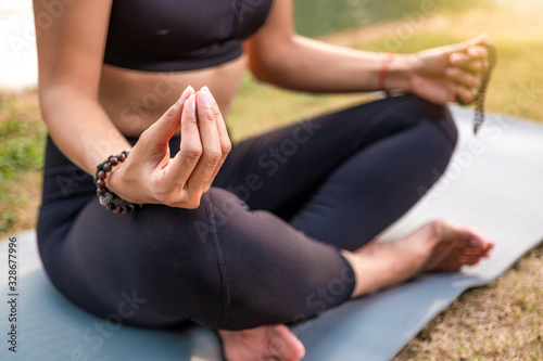 Woman sitting in yoga posture of buddha. Close up on hand holding asian beads or necklace with pearls